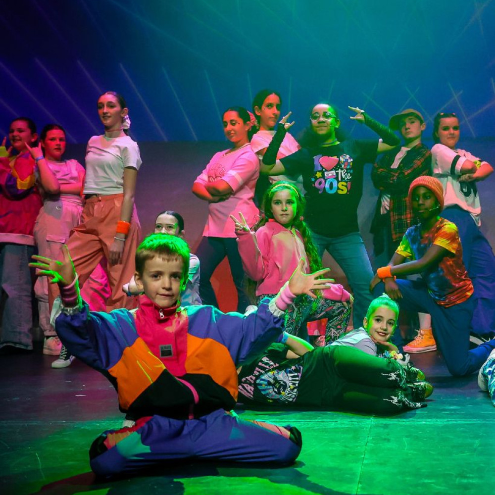 Group of Stagecoach Performing Arts students in colourful costumes posing on stage under vibrant lighting during a dance performance