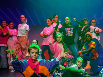 Group of Stagecoach Performing Arts students in colourful costumes posing on stage under vibrant lighting during a dance performance