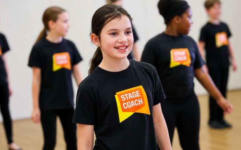 A smiling student takes part in a performing arts class while other students practise in the background.
