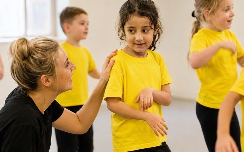 Teacher supporting a child during a group performing arts class