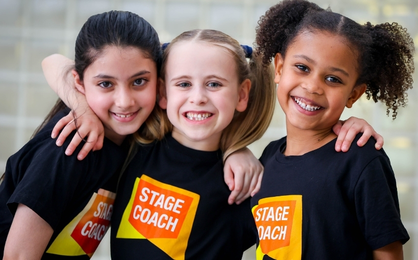 Three young Stagecoach students smiling with their arms around one another