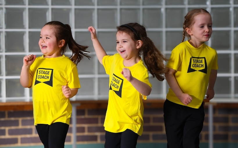 Three young Stagecoach students dancing together in yellow Stagecoach T-shirts
