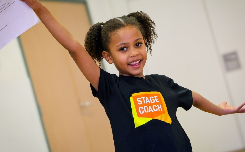 A young Stagecoach student performing with one arm raised during a drama or movement activity