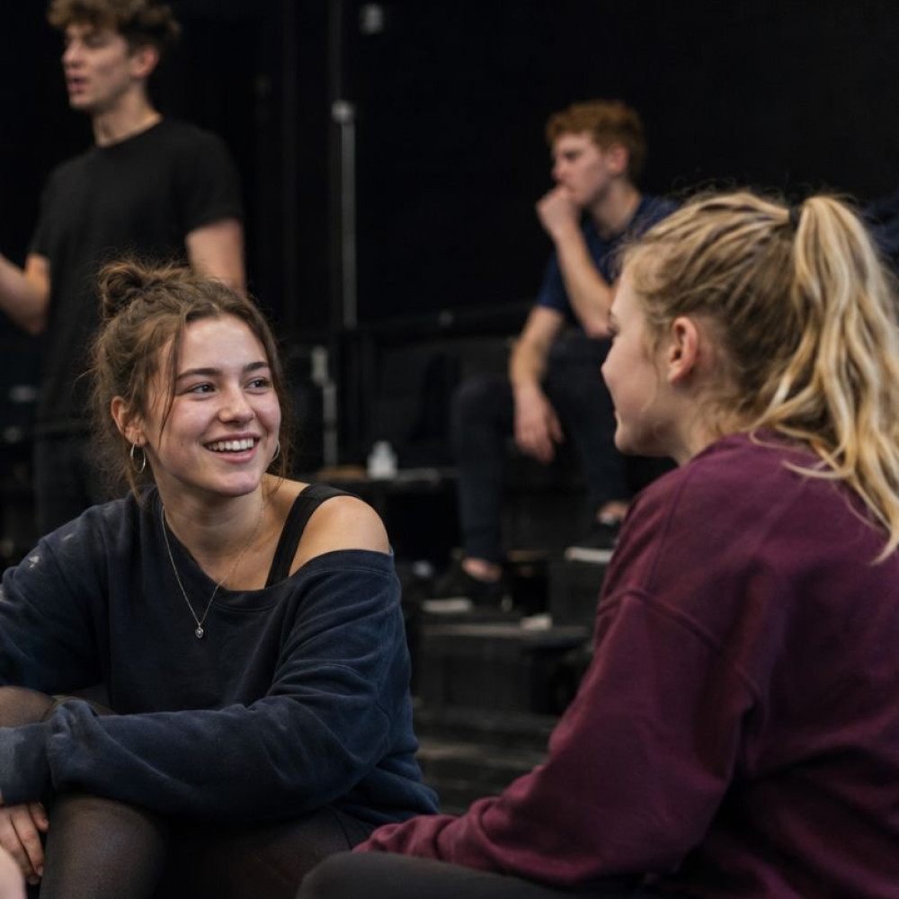 A small group of teenagers and young adults sitting together in a rehearsal studio and chatting during a performing arts class