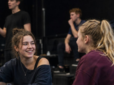 A small group of teenagers and young adults sitting together in a rehearsal studio and chatting during a performing arts class